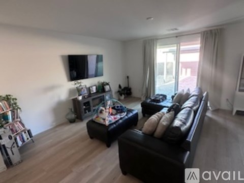 A living room with a black leather couch and a flat screen TV mounted on the wall.