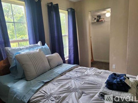 A bedroom with a bed, blue comforter, and a window with blue curtains.