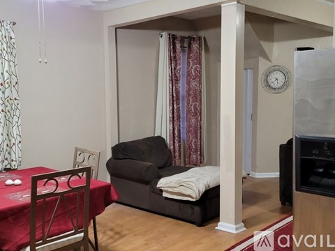 A living room with a sofa, a table with a red tablecloth, and a clock on the wall.