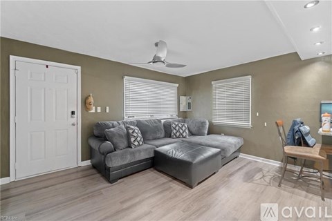 A living room with a grey couch and a fan on the ceiling.