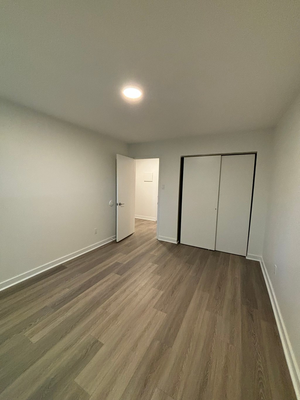 A room with a wooden floor and a white wall with a door.