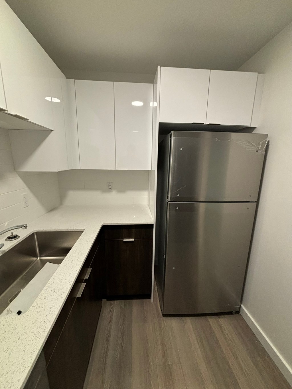 A kitchen with a stainless steel refrigerator and wooden floors.