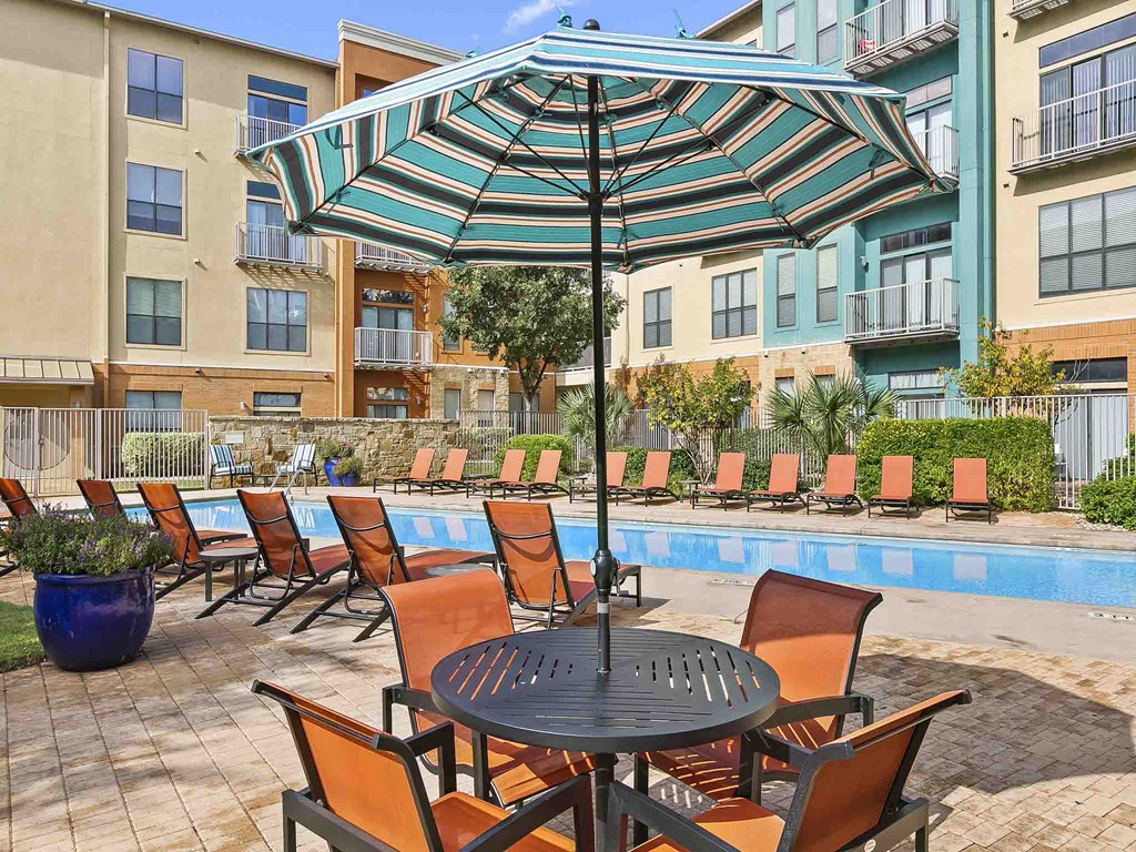 a table and chairs under an umbrella next to a swimming pool
