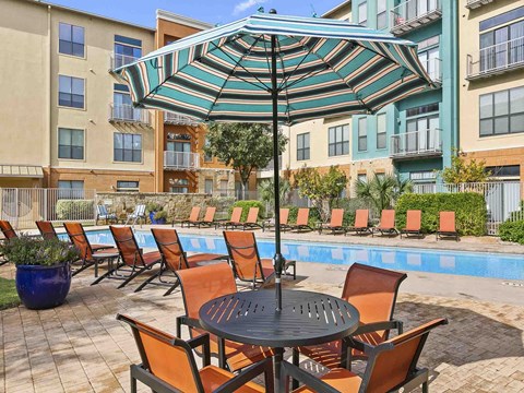 a table and chairs under an umbrella next to a swimming pool