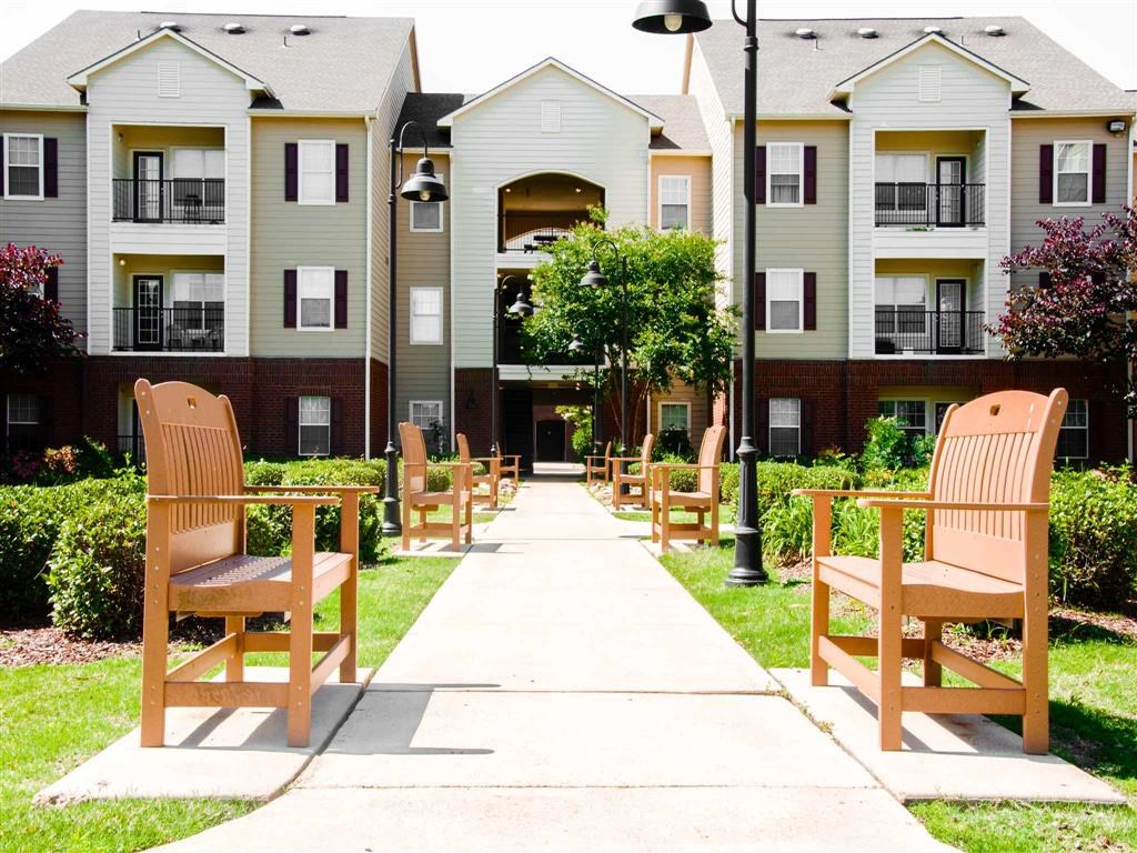 an empty sidewalk with wooden chairs in front of an apartment complex