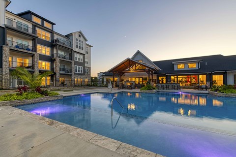 A large swimming pool in front of a building with a lit up fountain.