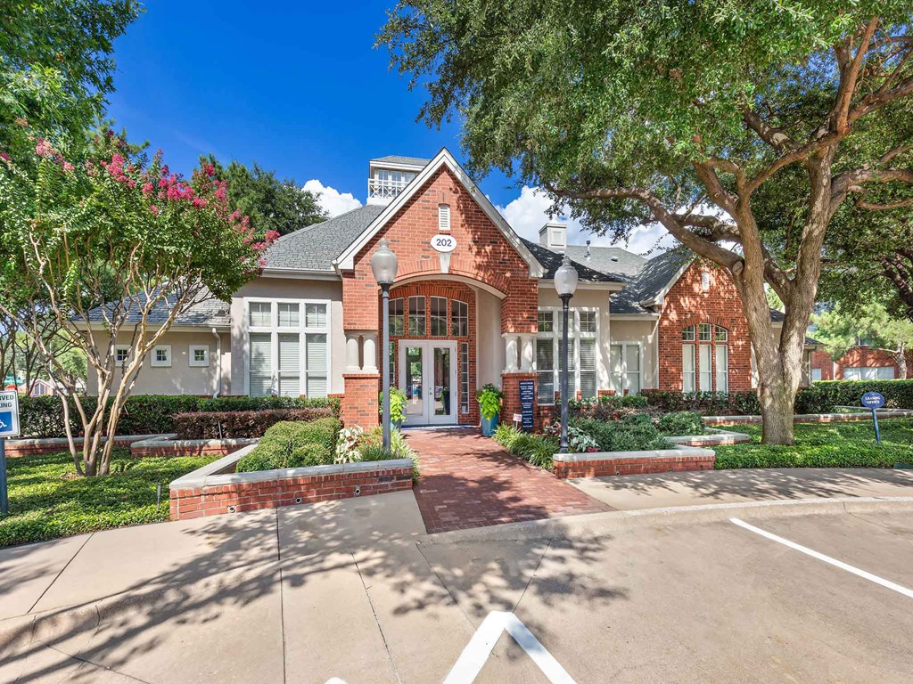 the front of a brick house with a driveway and trees