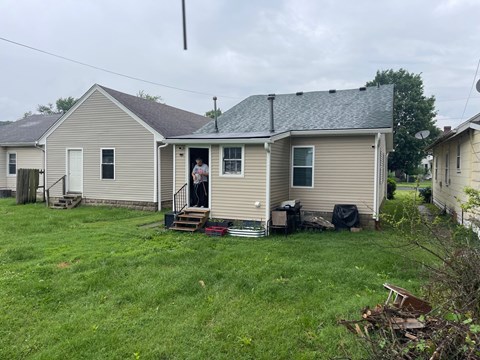 A house with a grey roof and a couple standing in the doorway.