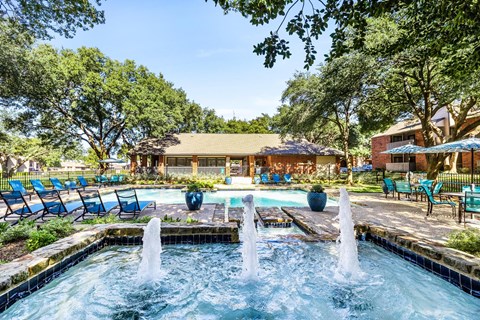 a pool with a fountain and chairs in front of a house