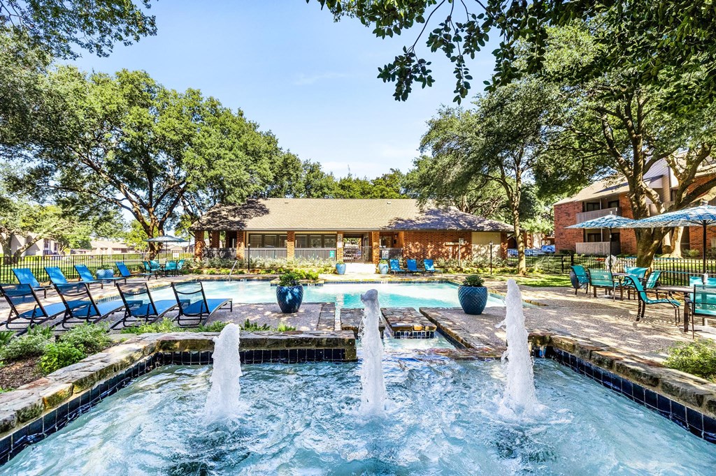a pool with a fountain and chairs in front of a house