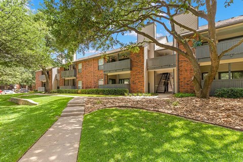 a sidewalk leading to an apartment building with green grass and trees