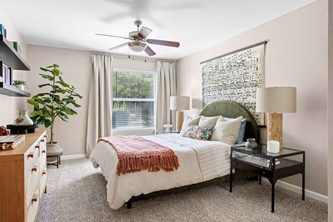 A bedroom with a bed, a ceiling fan, and a window with a view of trees.