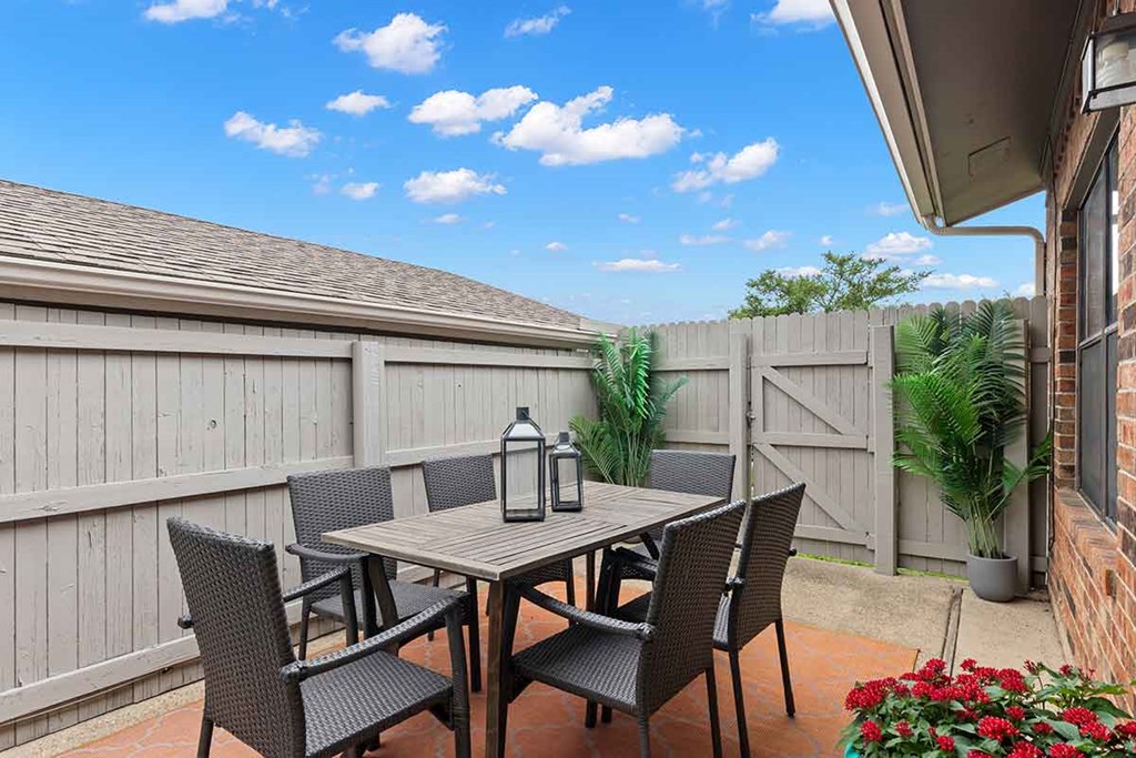 a patio with a table and chairs in front of a fence