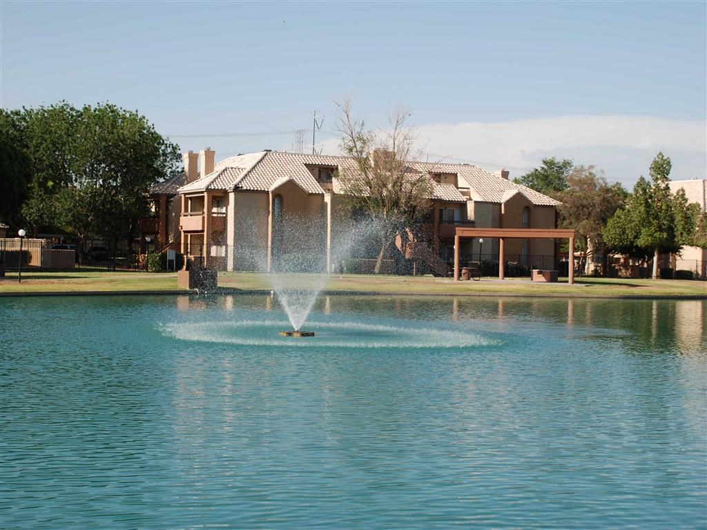 a fountain in the middle of a lake with houses in the background