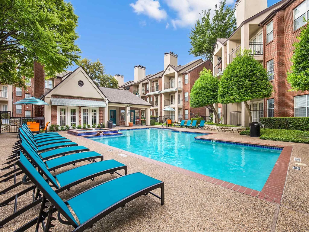 an outdoor pool with blue lounge chairs and an apartment building