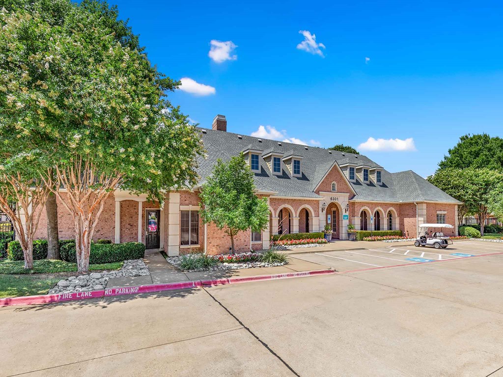 the front of a brick house with a driveway and trees
