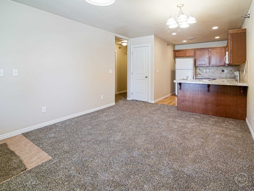 an empty living room and kitchen with wood cabinets and carpet