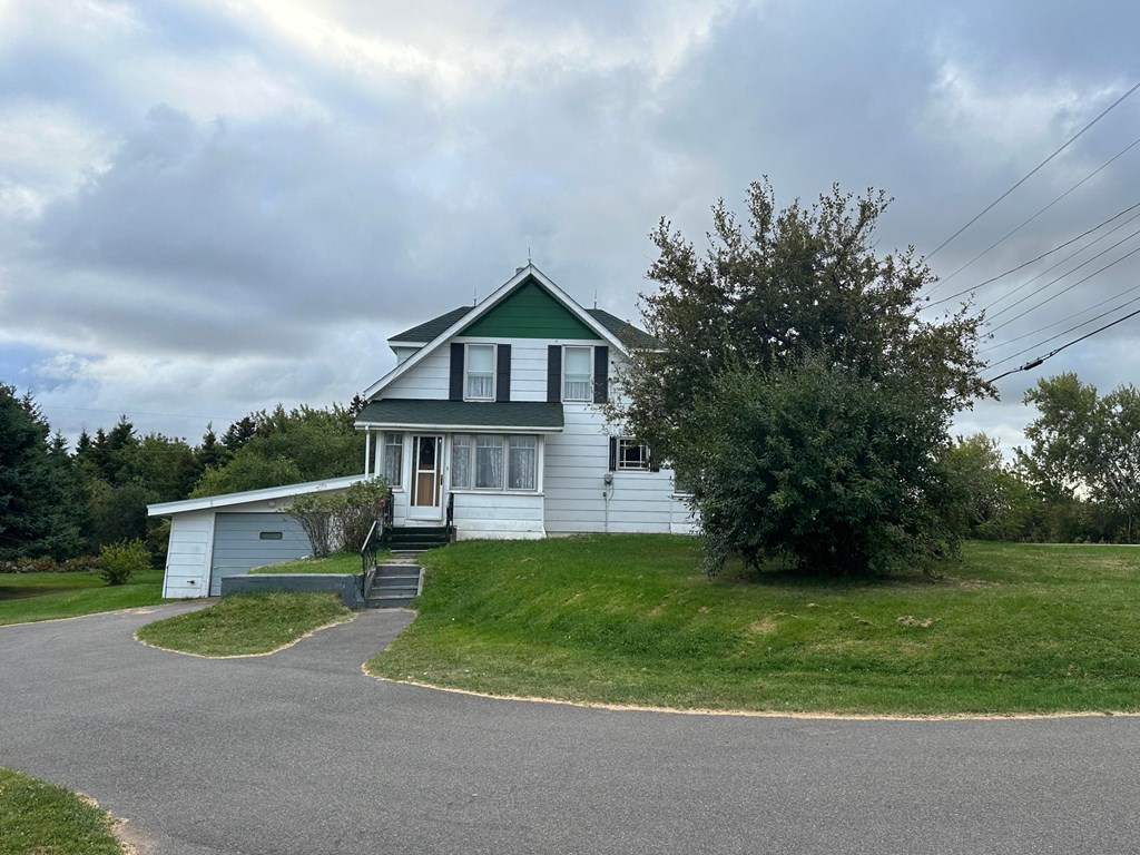 A house with a green roof and white walls is surrounded by a grassy lawn and a curved driveway.