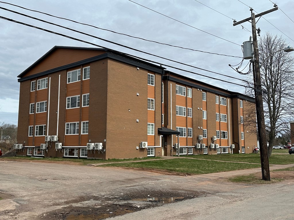 A brown and beige apartment building with a parking lot in front.