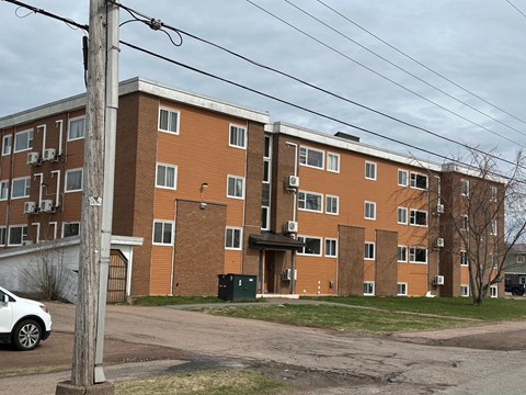 A large brick apartment building with a white car parked in front.