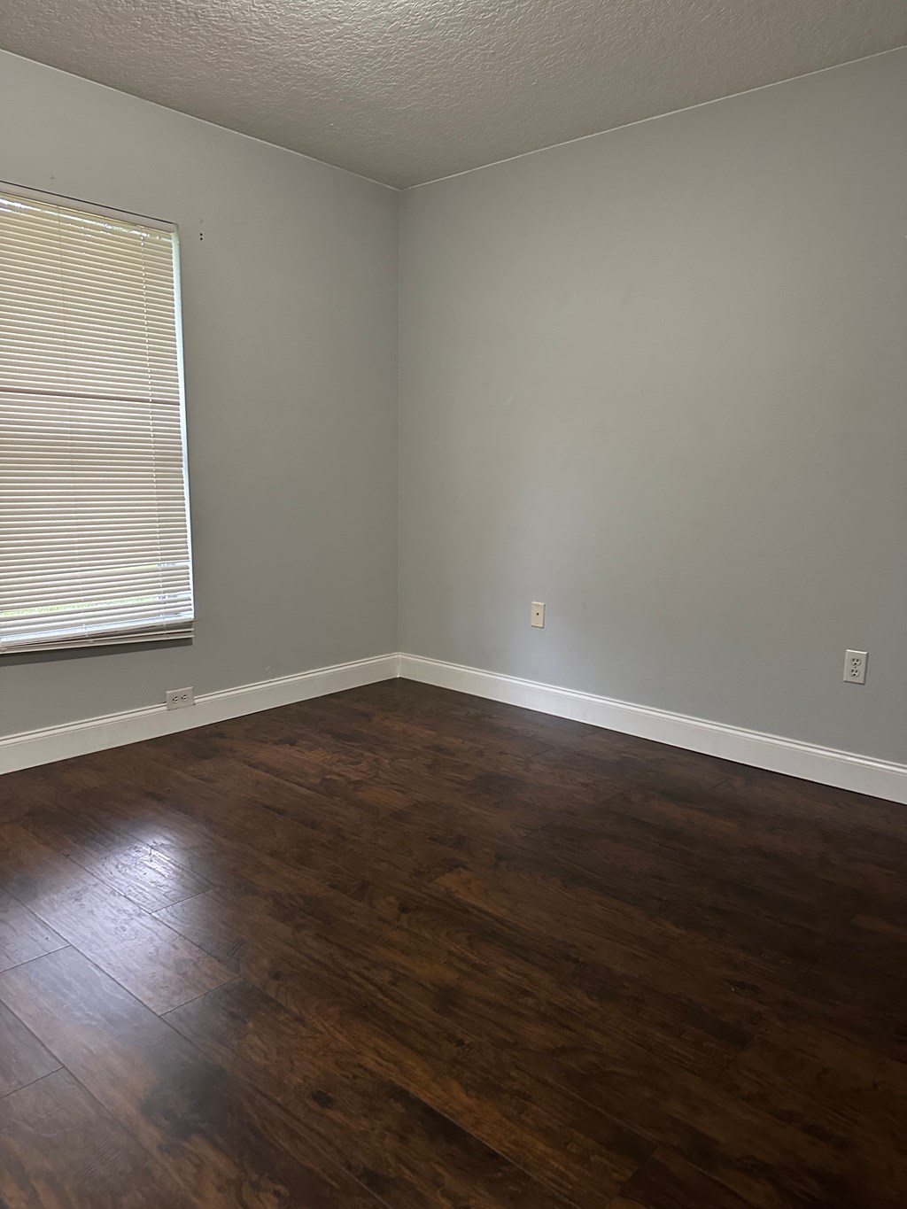 A room with wooden flooring and a window with blinds.