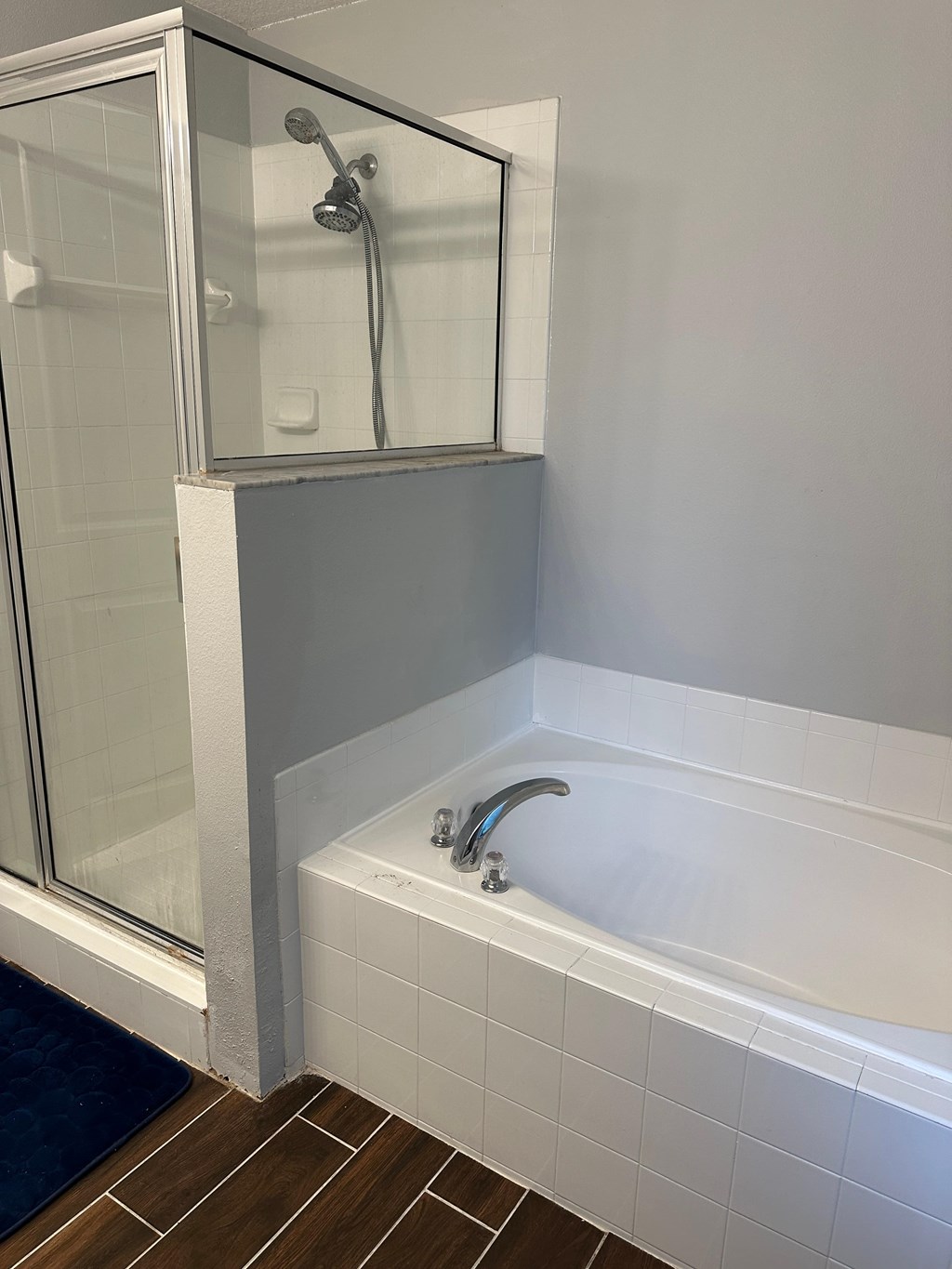 A white tiled bathroom with a glass shower door and a white bathtub.