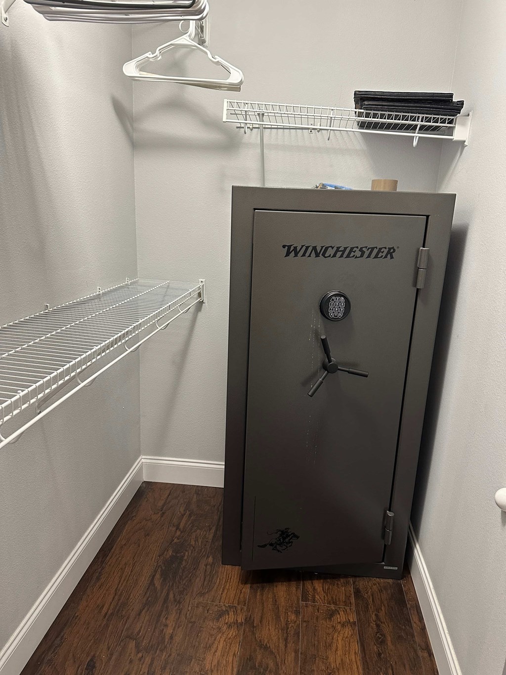 A Winchester safe is in a room with a white wall and a shelf above it.