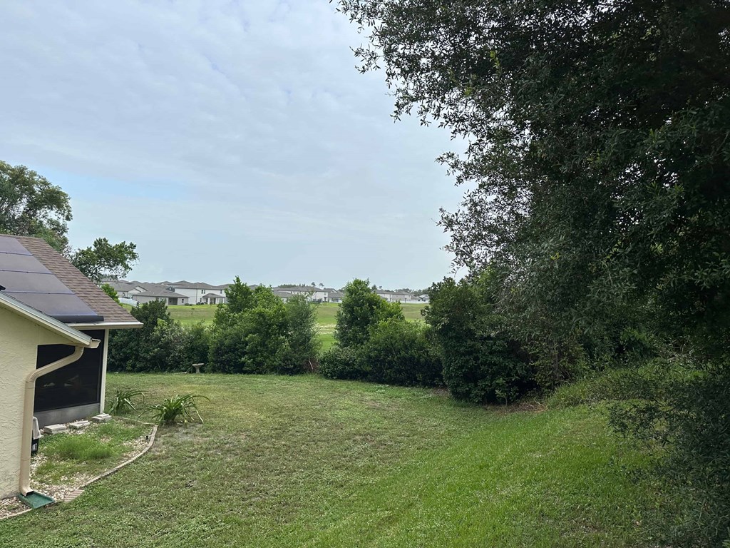 A house with a solar panel on the roof is surrounded by a grassy yard and trees.