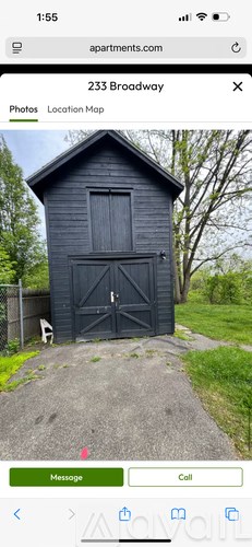A small black building with a door and a window is surrounded by greenery.