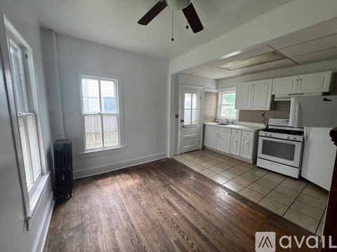 A room with wooden floors and a kitchen area with white appliances.