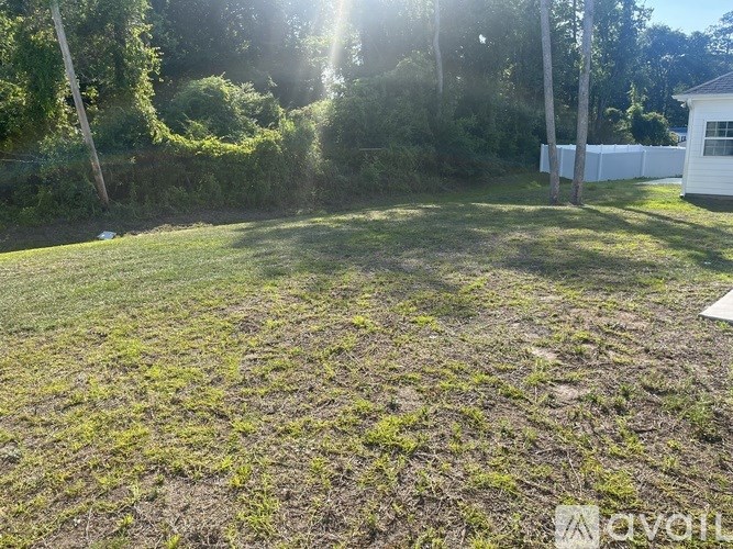 A backyard with a white fence and green grass.