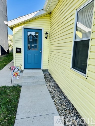 A yellow house with a blue door and a small flag on the front step.