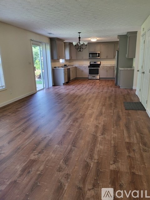 A room with wooden flooring and a kitchen area in the background.
