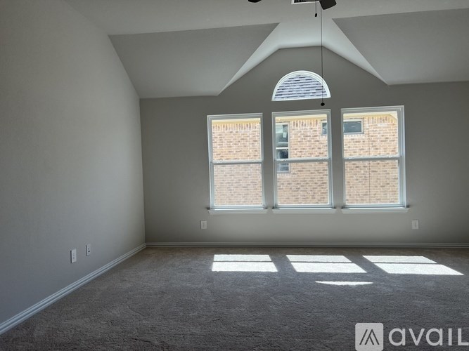 A room with a carpeted floor, a ceiling fan, and a large window with a view of a brick building outside.