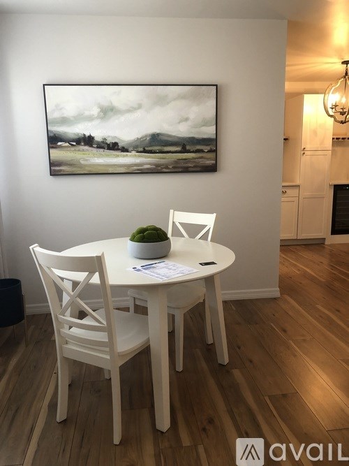 A white dining table with four chairs and a painting on the wall.