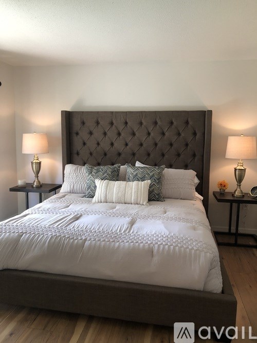 A bed with a white comforter and a dark headboard with tufting is flanked by two small tables with lamps on them.