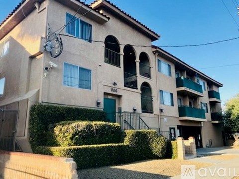 A beige apartment building with green shutters and a hedge in front.