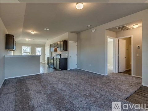 A spacious living room with a grey carpet and a flat screen TV mounted on the wall.