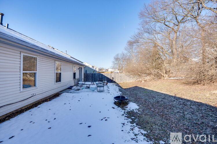 A house with a snow-covered ground and bare trees in the background.
