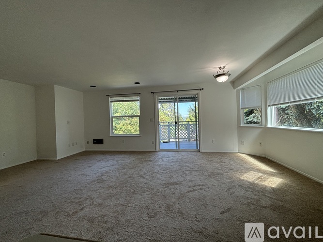 A spacious room with carpeted floor, a window, and a door leading to a balcony.