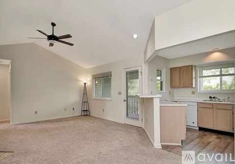 A spacious living room with a ceiling fan and a kitchen area in the background.