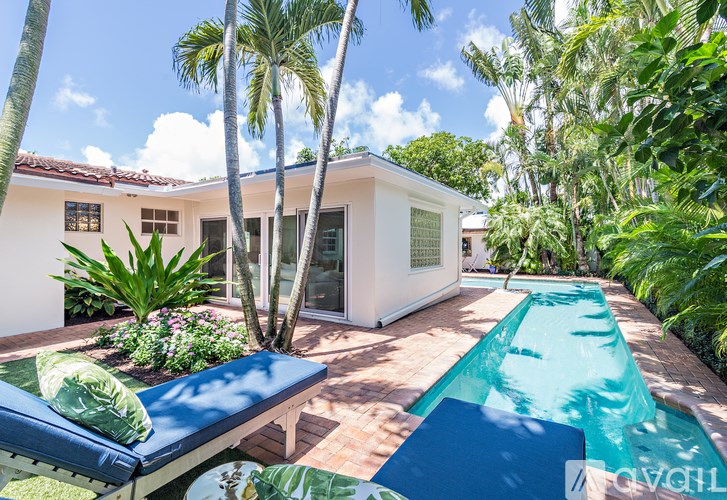 A pool in a backyard with a white house and palm trees.
