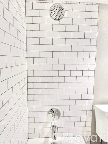 A white tiled shower with a shower head and a faucet.