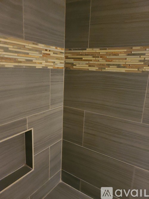A bathroom with a grey tiled wall and a brown tile strip.