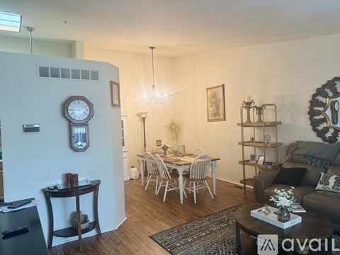 A living room with a dining table and chairs, a sofa, and a large clock on the wall.