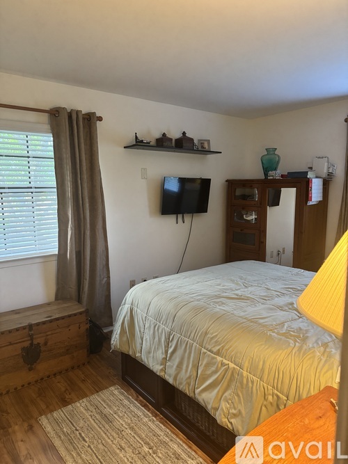 A bedroom with a bed, a TV, and a window with curtains.