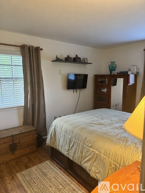 A bedroom with a bed, a TV, and a window with curtains.