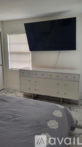 A bedroom with a bed, dresser, and a flat screen TV mounted on the wall.