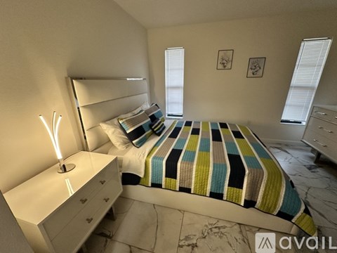 A bedroom with a bed, nightstand, and two windows.