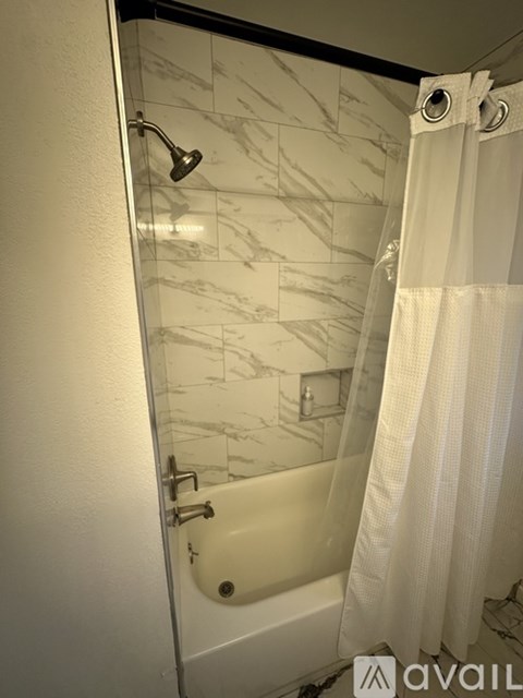 A bathroom with a marble tile shower and a white shower curtain.